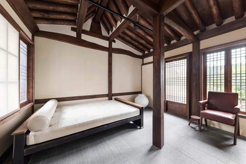Bedroom with exposed timber post-and-beam structure, gridded sliding doors and white daybed beneath vaulted ceiling