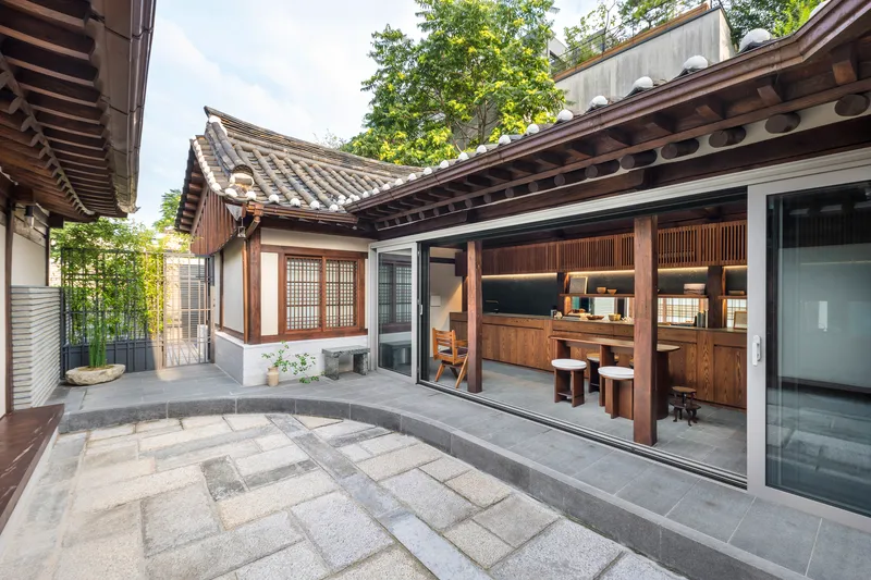 Courtyard view with grey stone pavers linking traditional tiled-roof structures to glazed interior spaces