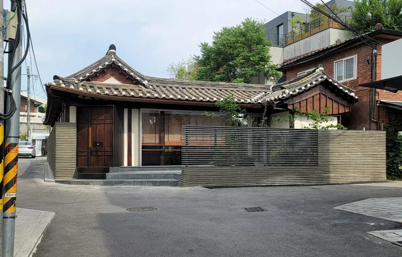 Corner view showing the ribbed metal perimeter wall and curved tile roofline from the street