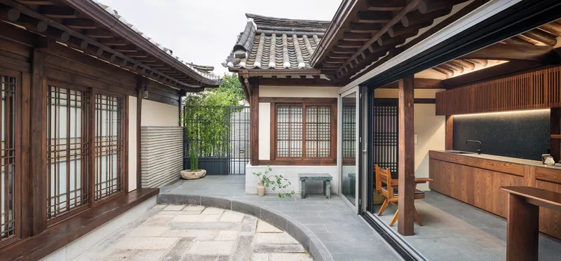 Courtyard framed by timber eaves and lattice screens with planted bamboo and stone bench