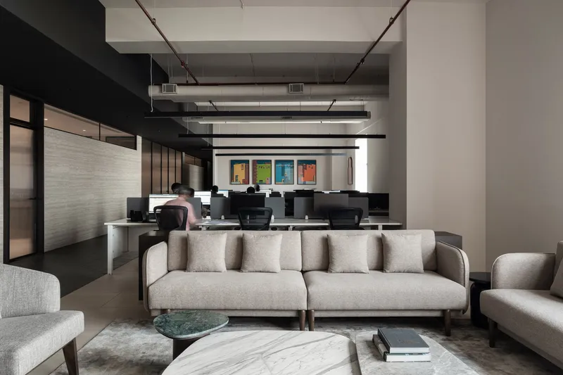 Lounge area with sofas and a marble coffee table overlooking workstations with exposed services
