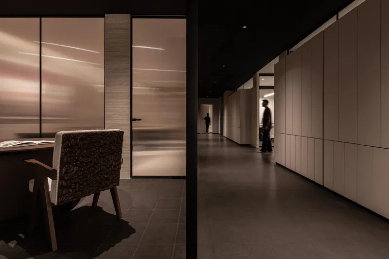 Long corridor with translucent glass partitions and light wood paneling under dramatic artificial lighting
