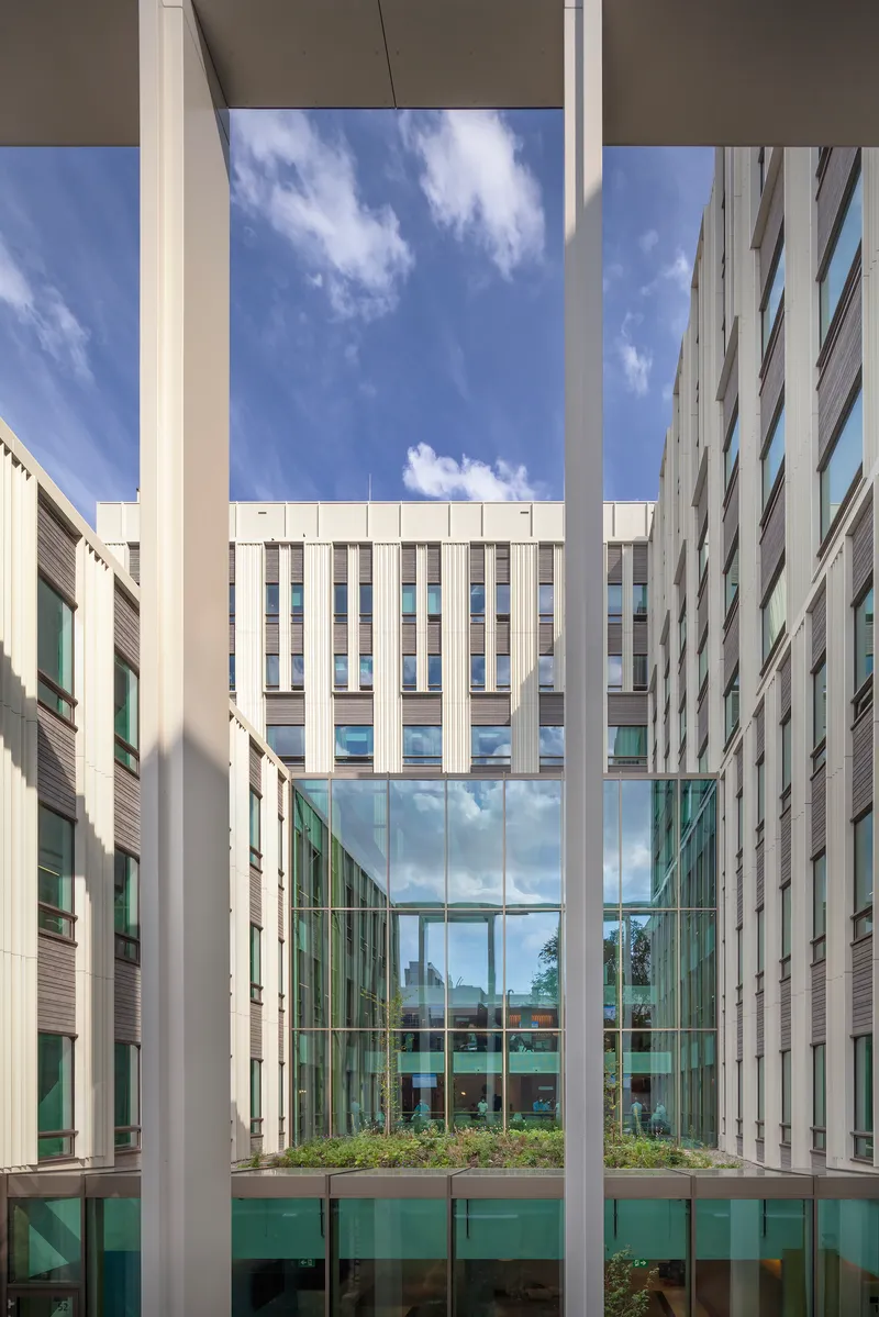 Multi-story atrium framed by vertical white fins and glass-walled bridge under afternoon sunlight