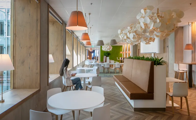Dining area with round white tables, timber-paneled walls and pendant lighting beside glazed curtain wall