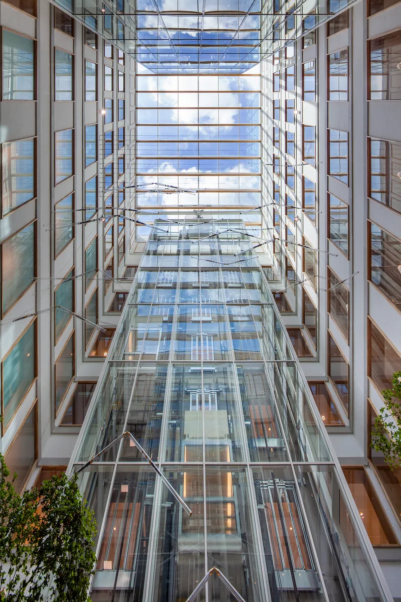 Upward view through a multi-story glass-roofed atrium flanked by office floors and green plants below