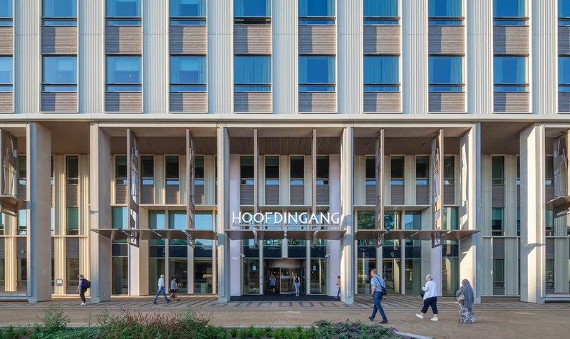 Ground-level entrance colonnade with vertical fins above and pedestrians crossing the plaza