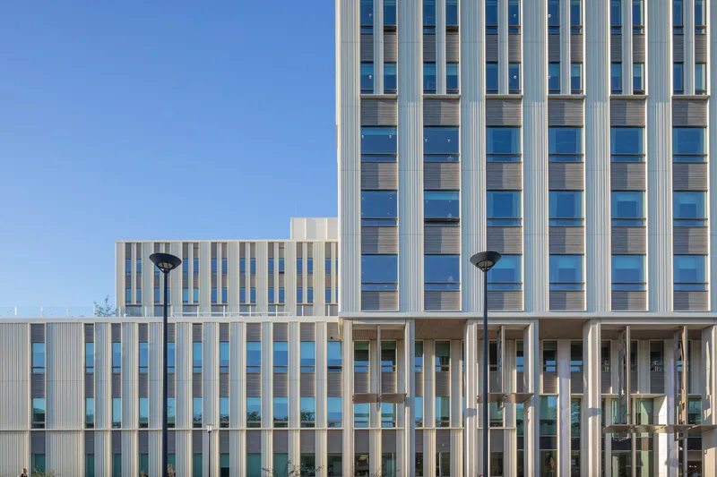 Facade detail showing vertical white fins alternating with glazed and timber-clad window bands