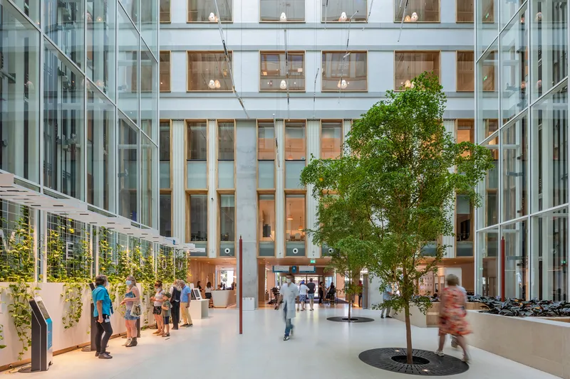 Interior atrium with central tree, planted beds, and visitors moving through the glazed space