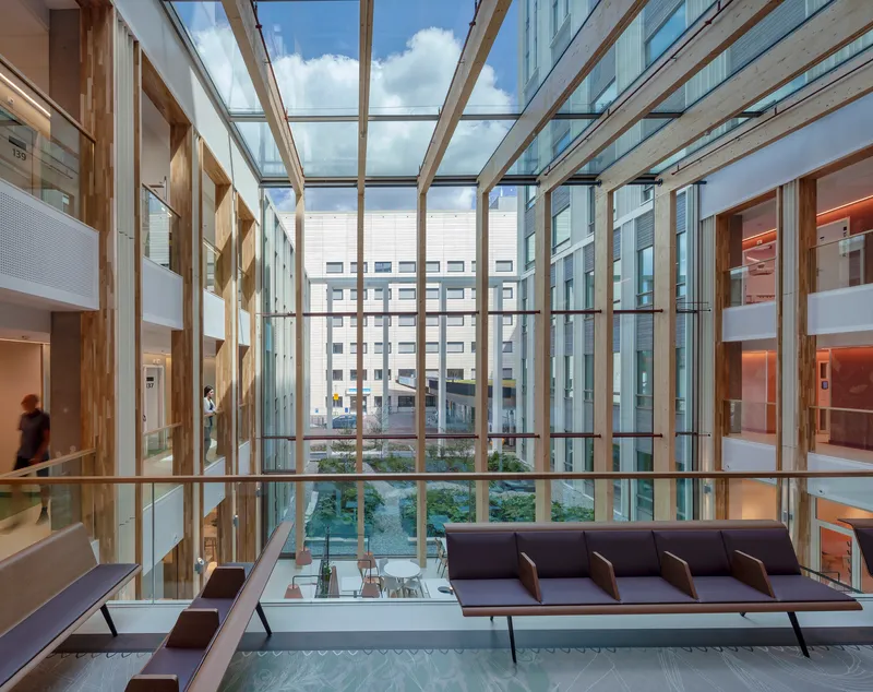 Lounge seating with dark upholstery facing floor-to-ceiling glazing overlooking a landscaped courtyard between buildings