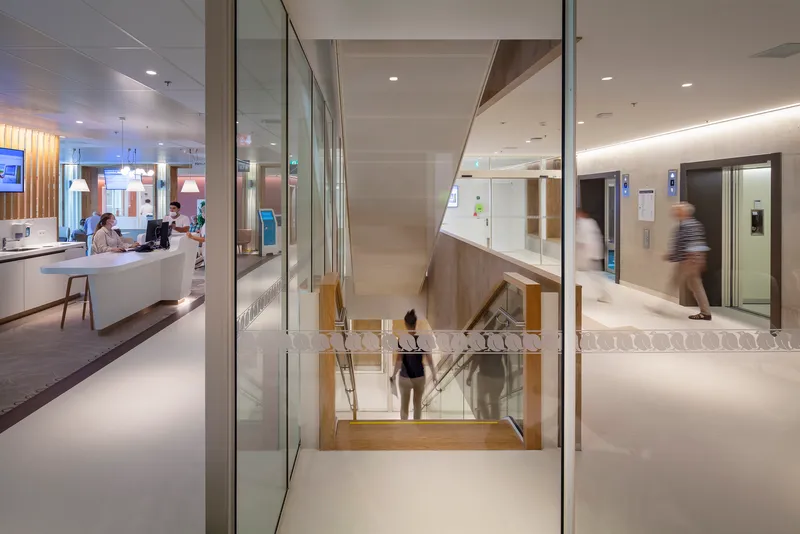 Timber staircase descending between glass partitions with people in motion near elevator banks