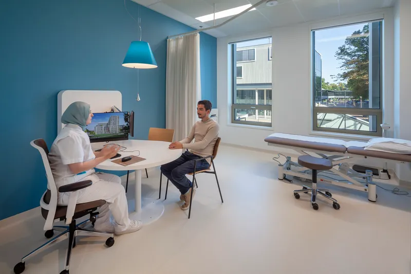 Consultation room with pale blue walls and tall windows overlooking trees outside