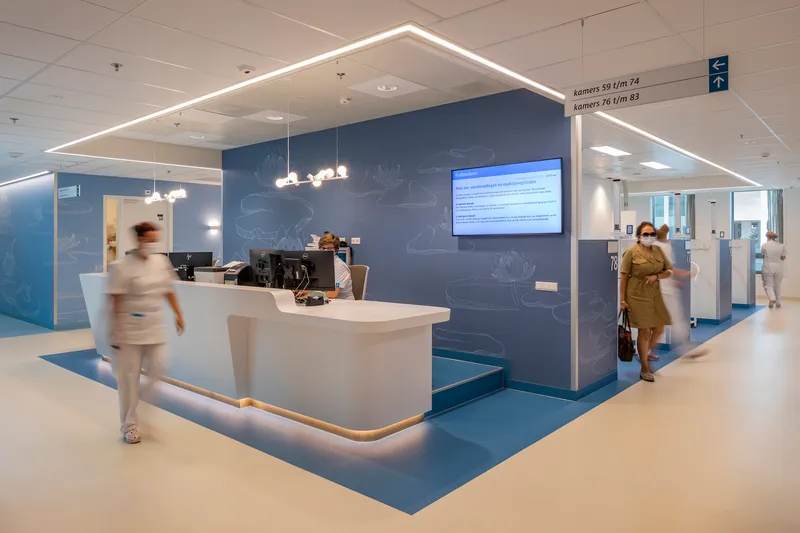 Reception desk under a house-shaped lighting canopy with staff and visitors passing through