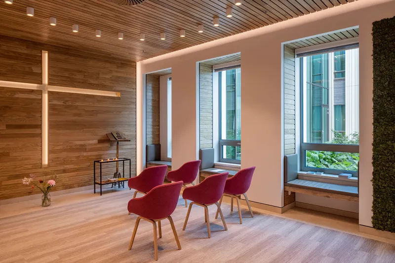 Chapel space with timber slat ceiling, wooden cross, and red upholstered chairs