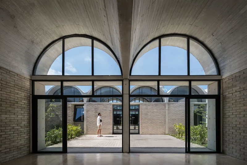 Interior view through arched glazing showing courtyard with figure walking across sunlit paving