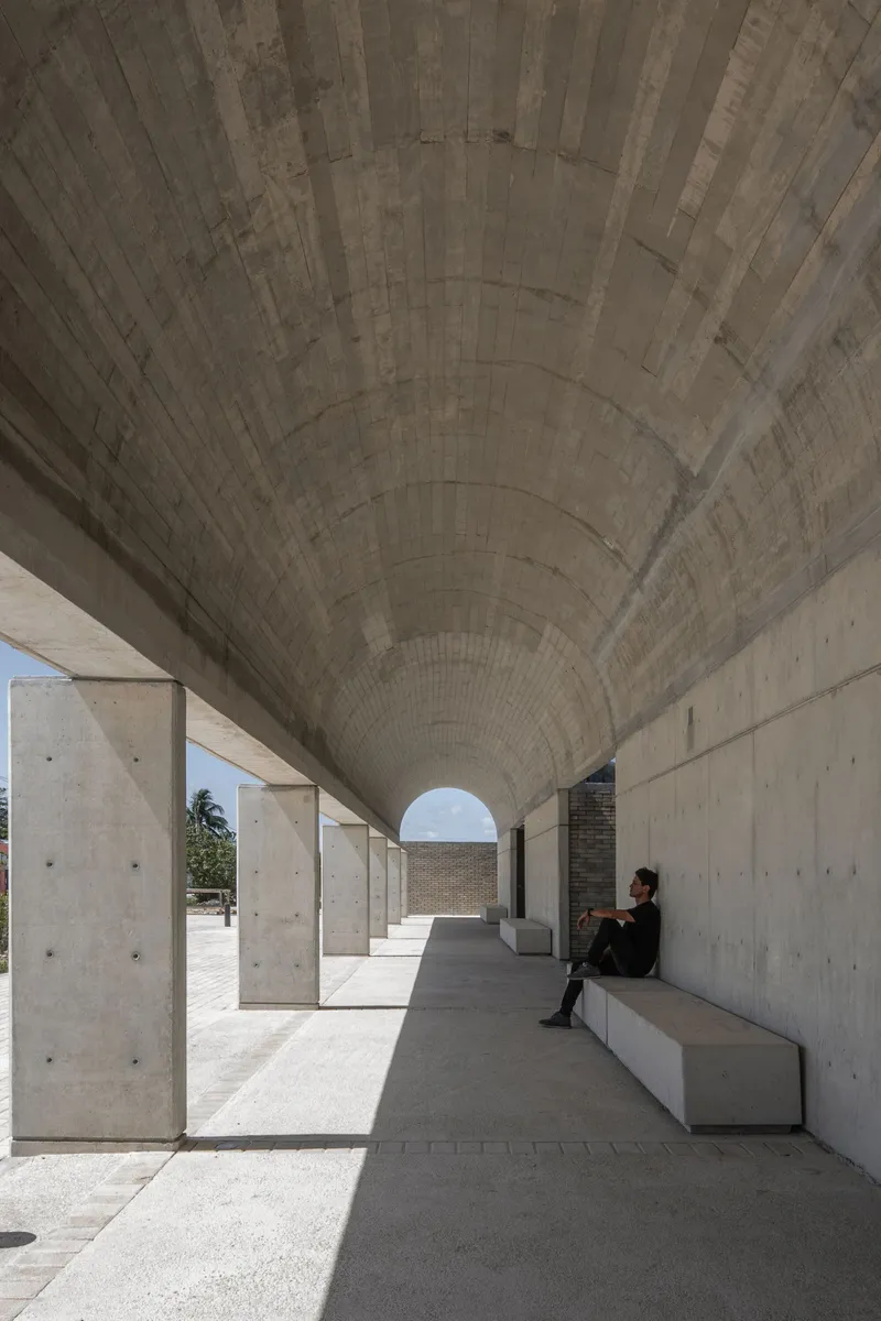 Barrel-vaulted concrete colonnade with person seated on bench in bright daylight