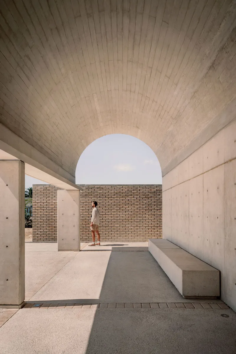 Covered passageway with board-formed concrete vault ceiling and circular opening framing a brick wall