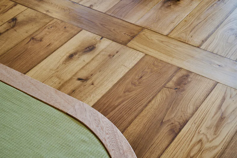 Close-up of reclaimed oak flooring in varied tones meeting the curved edge of a tatami platform