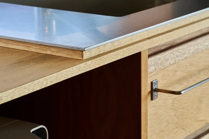 Detail of stainless steel countertop edge meeting an oak drawer front with inset pull hardware