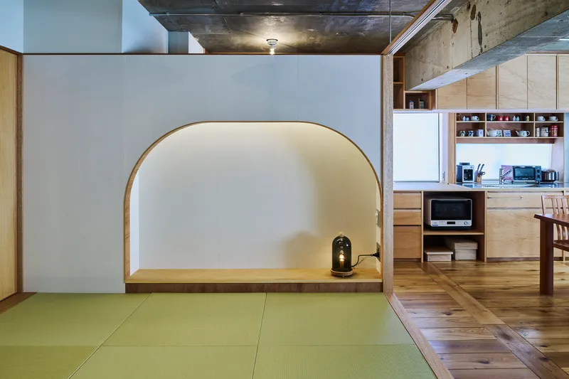 Raised tatami alcove with arched timber frame opening onto the kitchen and dining area beyond