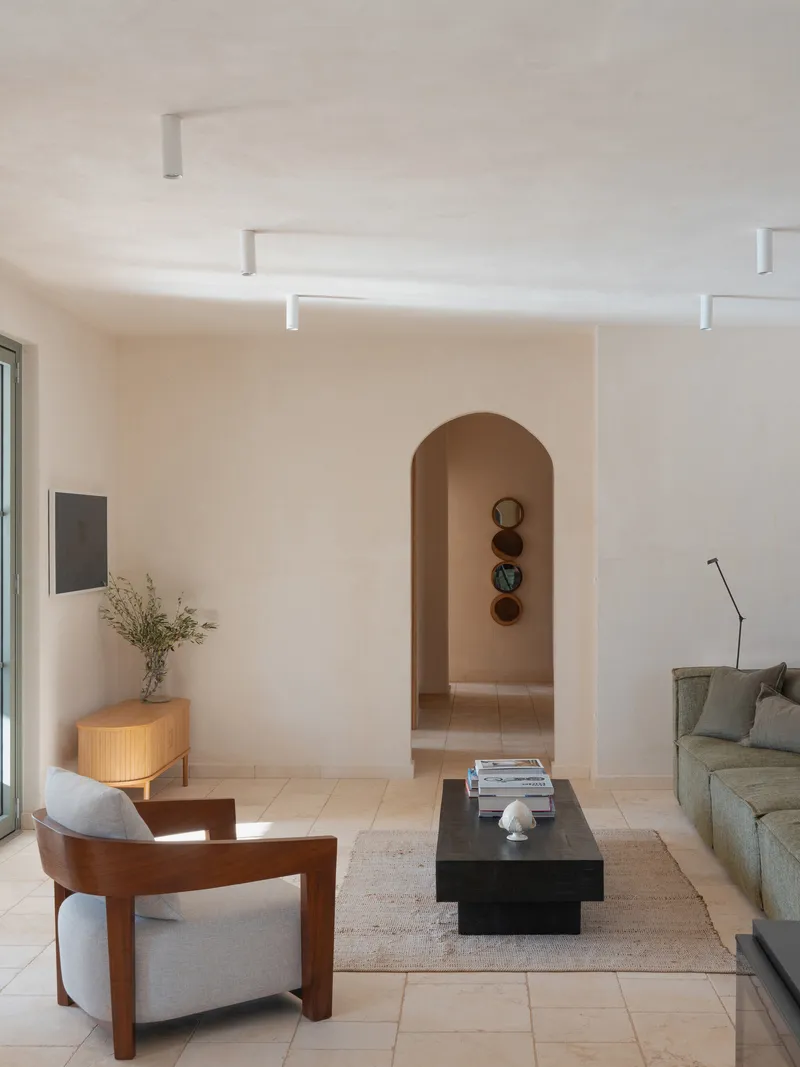 Living room with arched passage and square-profile pendant lights casting afternoon sun across limestone tile floor