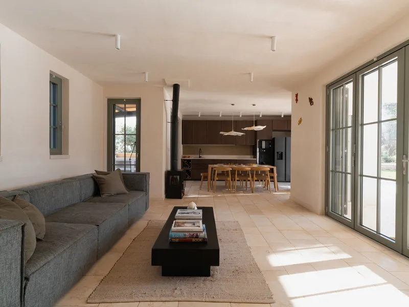 Open-plan living space with stone tile floor receiving afternoon sunlight from glazed doors