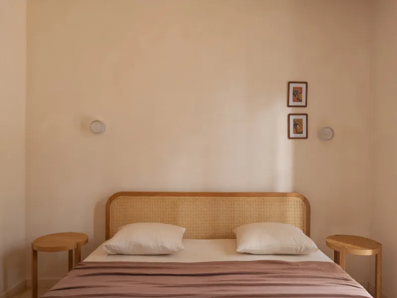 Bedroom wall with cane headboard and two framed artworks above cylindrical timber side tables