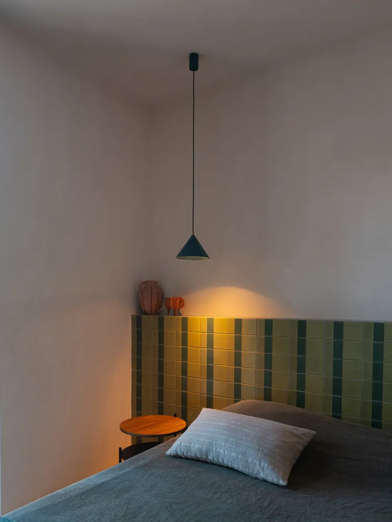 Bedroom with vertically striped green tile headboard and cone pendant light casting warm glow