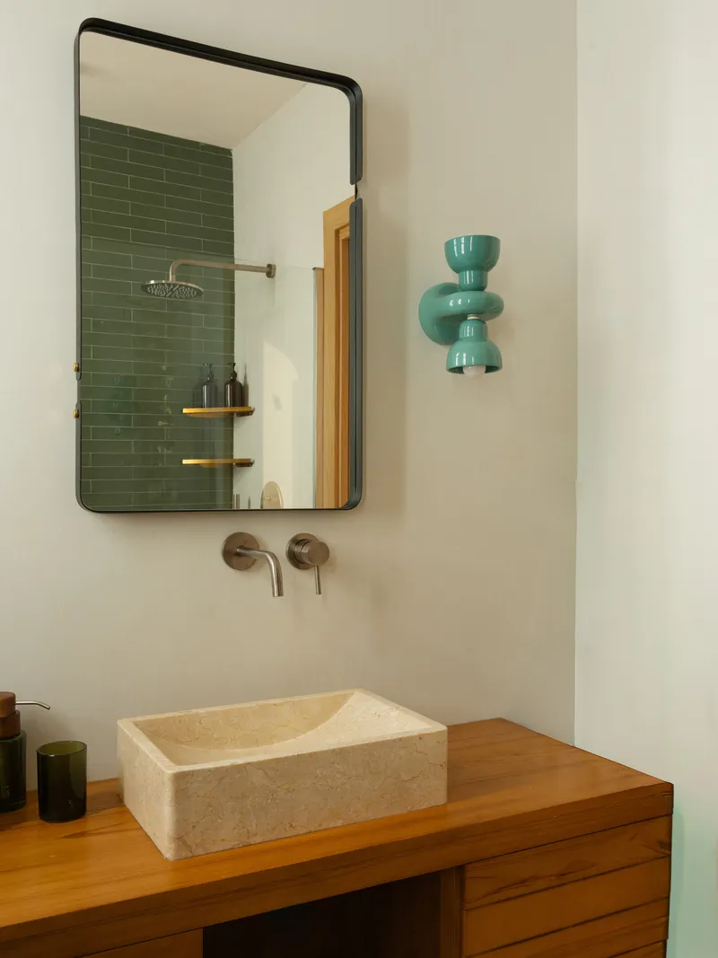 Bathroom vanity with limestone vessel sink on timber cabinet, mirror reflecting green subway tile shower