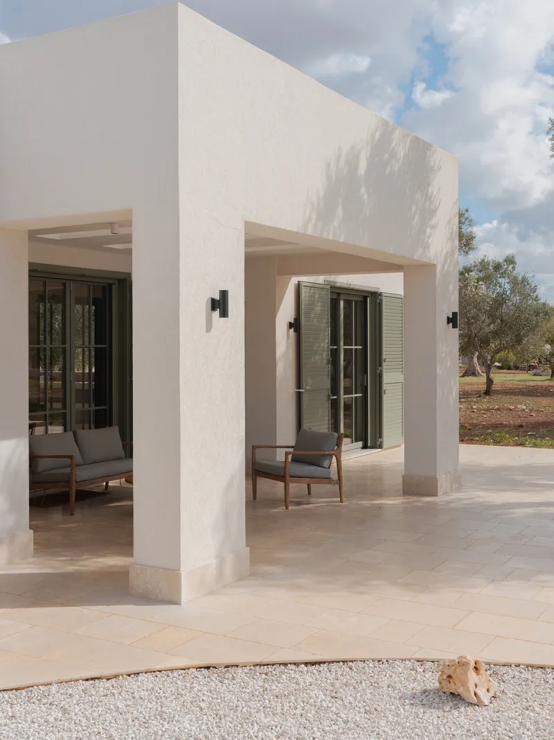 Covered terrace with white columns and stone paving opening to an olive grove