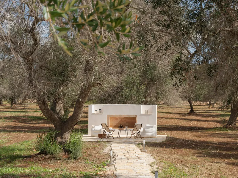 Freestanding white outdoor kitchen with arched opening in an olive grove under scattered clouds