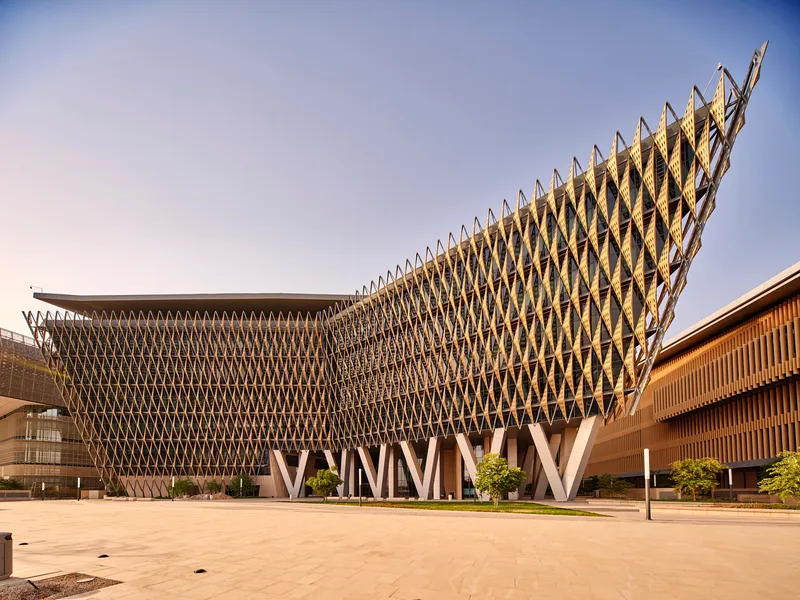 The curving diamond-patterned timber screen rising above a paved plaza with young trees