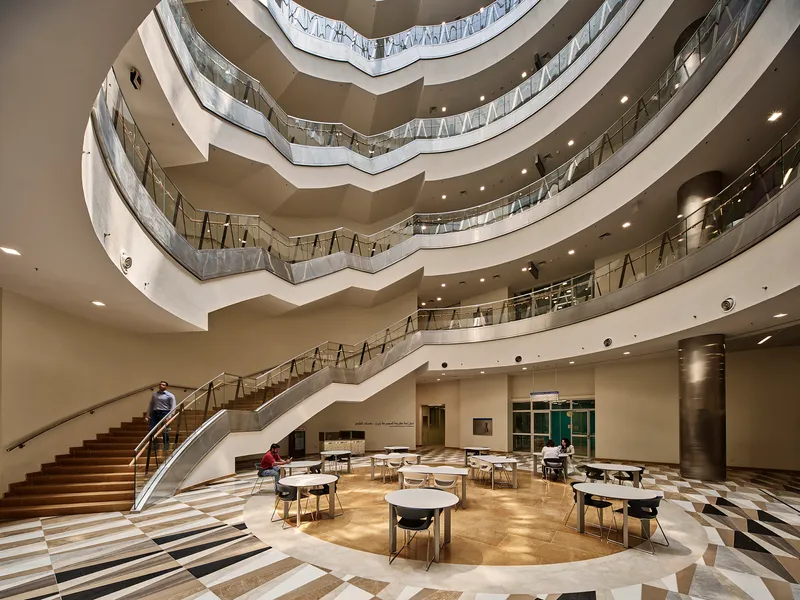 Interior atrium with spiraling floor plates, grand staircase, and round cafe tables on patterned stone floor