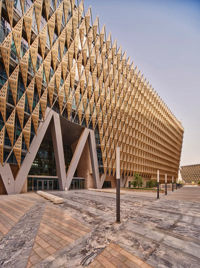 Entry facade with branching concrete columns beneath the layered timber lattice screen at dusk