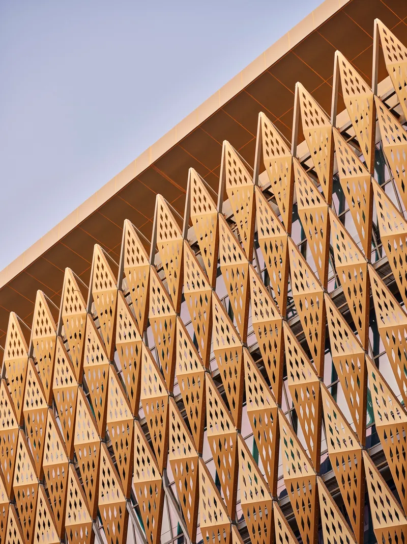 Perforated timber facade with zigzag screens creating a repetitive triangular pattern in afternoon light