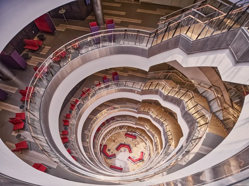 Looking down into spiral atrium void with red seating and timber-lined balconies
