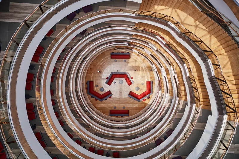 Overhead view of concentric atrium balconies surrounding hexagonal ground floor with red furniture