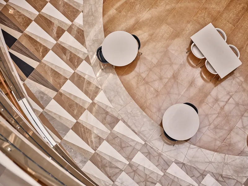 View down onto marble floor with round tables and diagonal shadow patterns from skylight