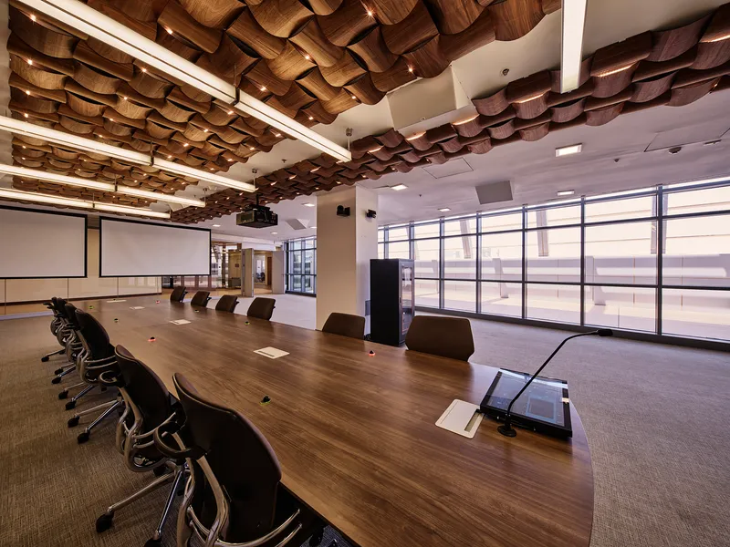 Conference room with long timber table and sculptural woven ceiling panels above glass curtain wall