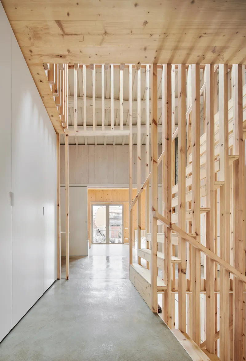 Corridor view through the slatted timber stairwell toward a glazed rear doorway