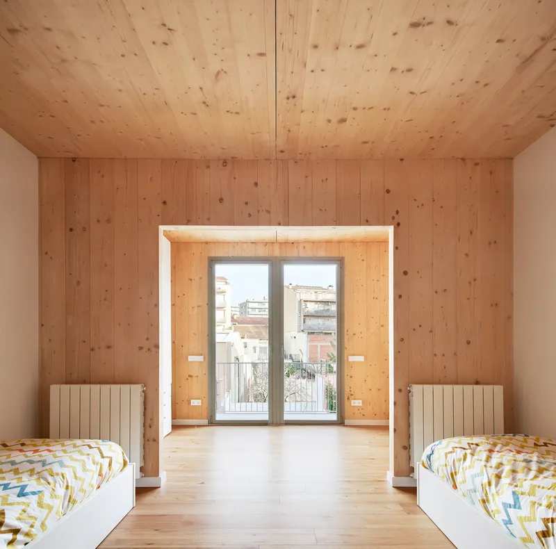 Bedroom with twin beds flanking deep timber-lined window opening with radiators and balcony access