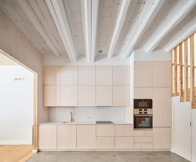 Light plywood kitchen cabinetry beneath exposed timber ceiling beams painted white