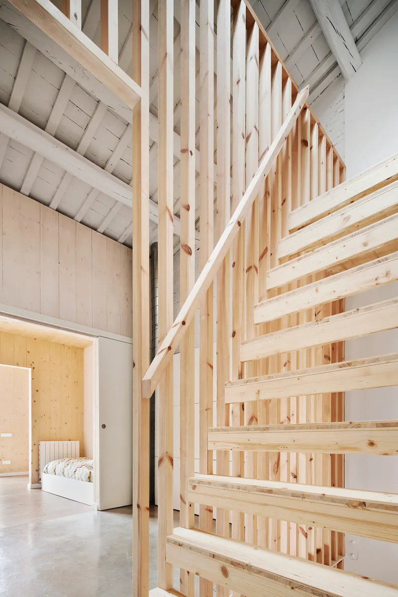 Open timber slat staircase rising between white walls under painted beam ceiling