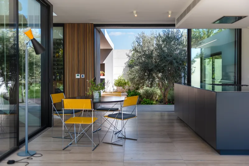 Open living space with yellow folding chairs framing a view to an interior courtyard with olive tree