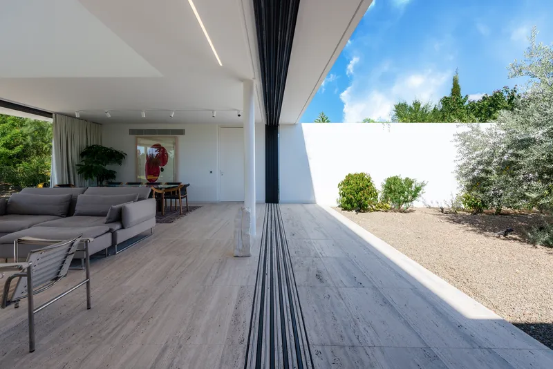 Sliding glass wall fully retracted opening the living room to a gravel courtyard with planted shrubs