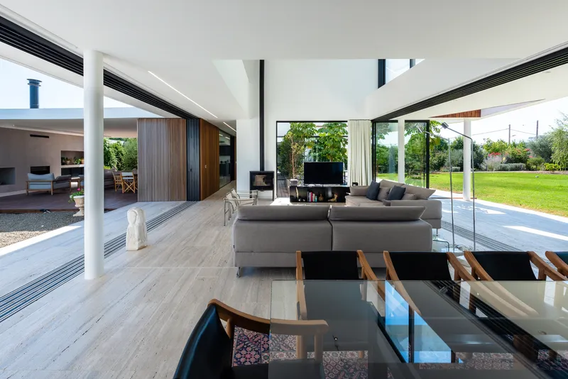 Open-plan living space with white columns and glass thresholds connecting to lawn and courtyard beyond