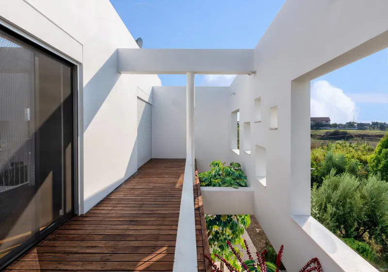 Rooftop terrace with timber decking and planted beds framed by white perforated walls under blue sky