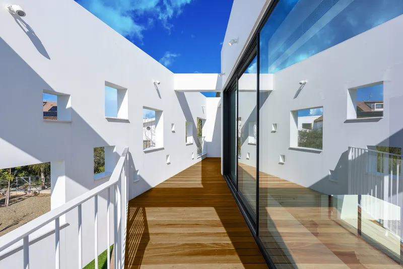 Upper-level timber deck corridor with perforated white screen walls casting geometric shadows in bright sunlight