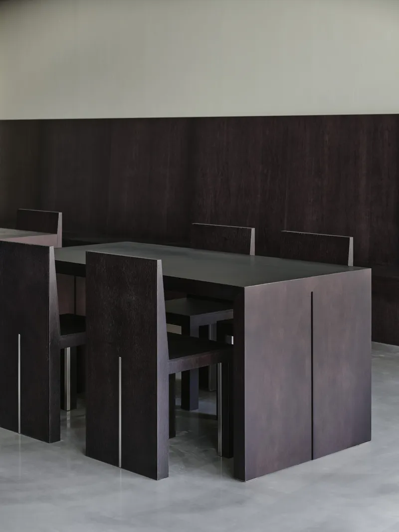 Close-up of black wood table and chairs against a dark paneled wall in even light