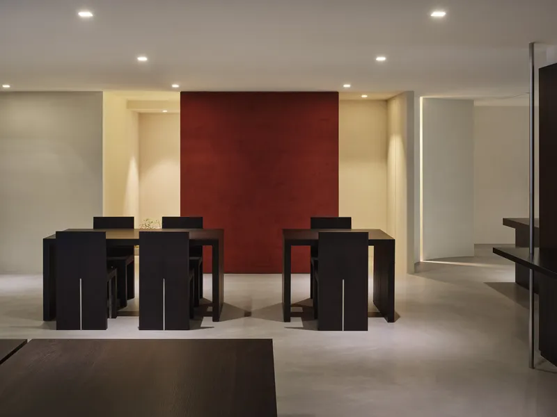 Multiple black dining tables arranged before a deep red accent wall in a pale interior
