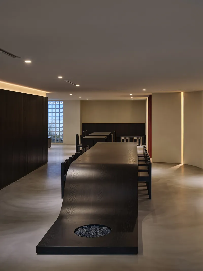 Long curving black table with circular planter cutout beneath cove lighting and translucent glass blocks